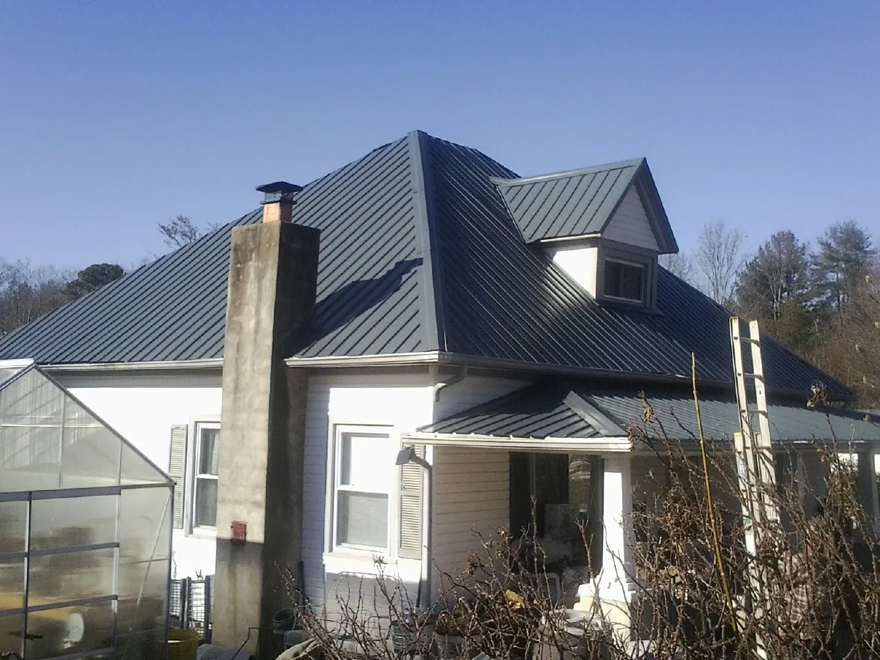 Dark blue standing seam metal roof on a white farmhouse with dormer — Slate & Tile Roof Repair by Roofing Brothers in Marlin
