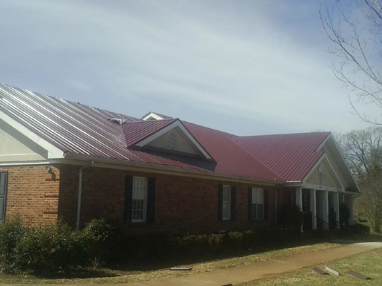 Red metal roof with gabled entries on a long brick building, from a Hail Damage Roof Repair job in Marlin