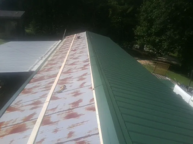 Old rusted panels beside newly installed green metal roofing — Wind Damage Roof Repair by Roofing Brothers in Marlin