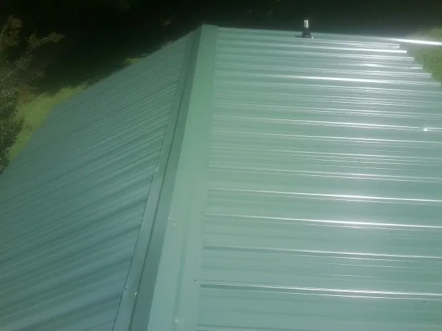 New green metal panels meeting at the ridge of a roof — Flat Roof Repair work by our crew in Marlin