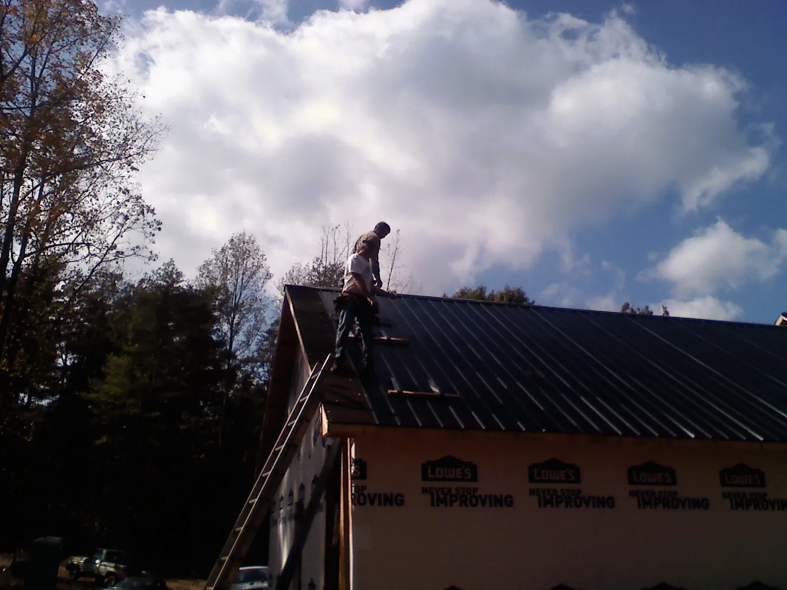 Roofer fastening dark metal panels high against a cloudy sky, from a Roof Inspection job in Marlin
