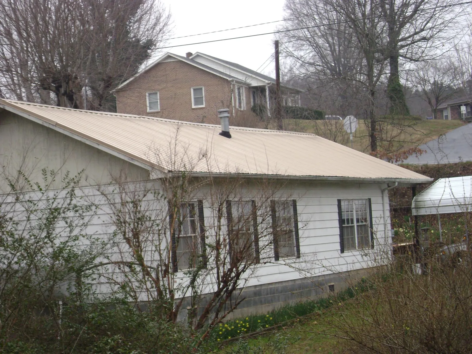 Tan metal roof on a white sided house set into a hillside — Commercial Roofing by Roofing Brothers in Marlin