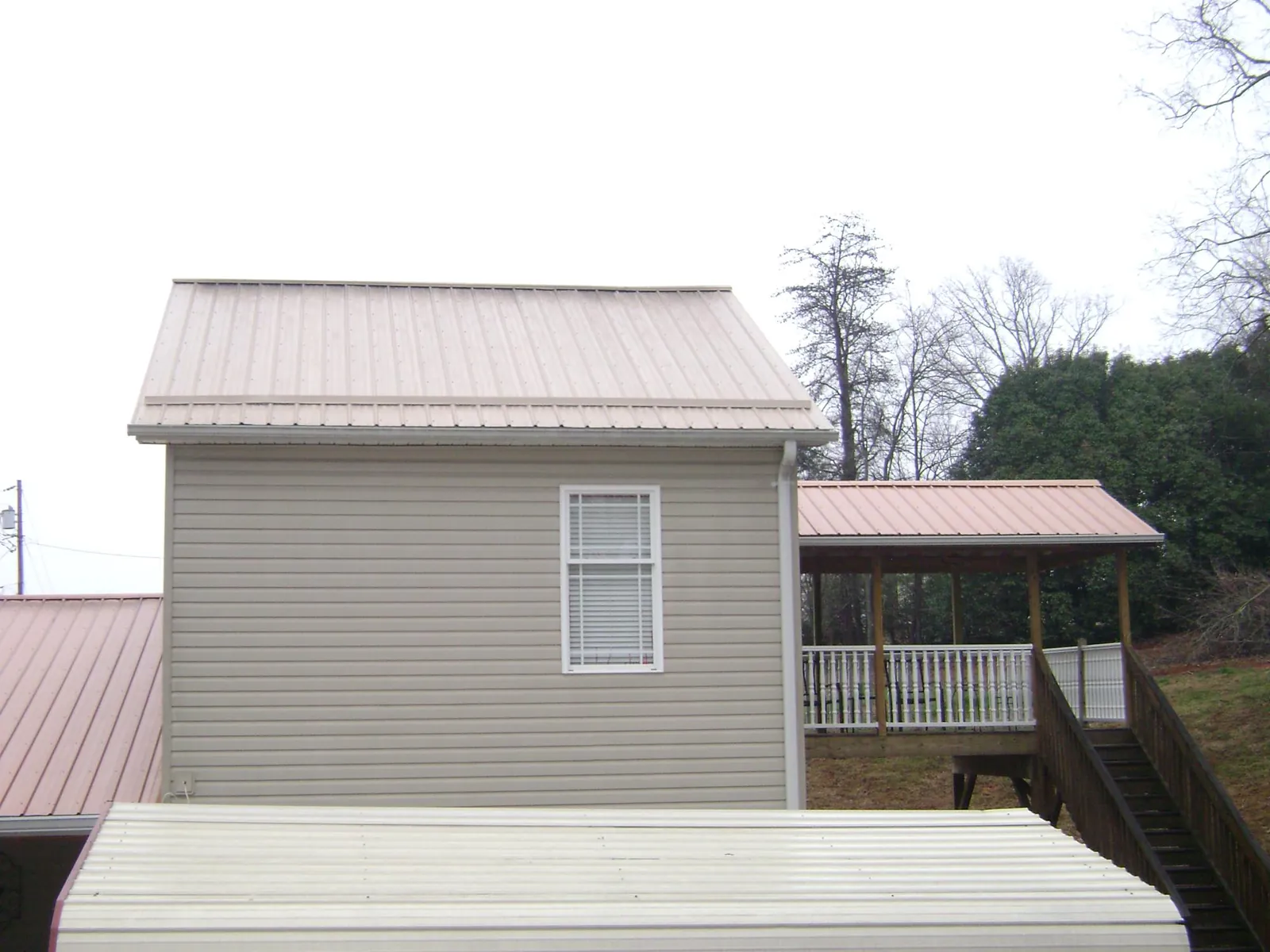 Tan metal roofs on a two story addition and attached porch, from a Roof Replacement job in Marlin